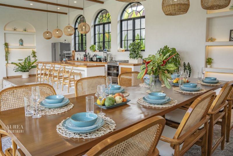 The dining room of the villa with a table, cutlery, blue plates, and plants, floor with wooden decor.