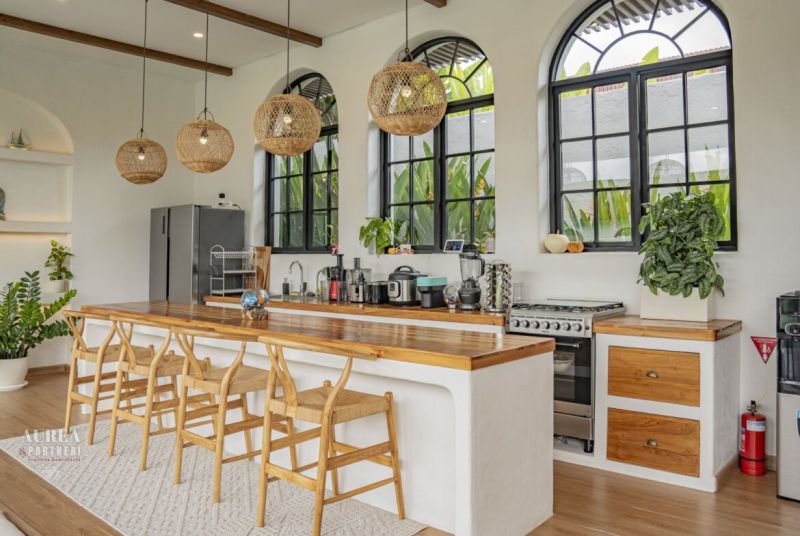 A kitchen in a villa with a bar counter, wooden chairs, and large windows.
