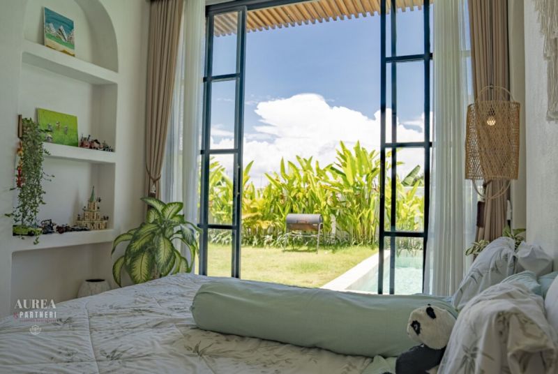 Bedroom in a villa with a view of the garden and pool, decorated with plants.