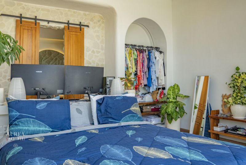 A bedroom in a villa with a bed, green plants, and an open wardrobe.
