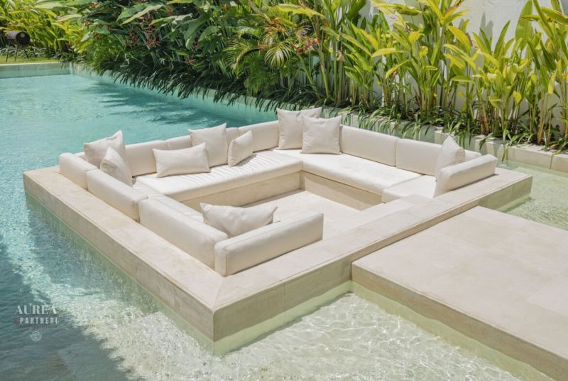 Seating in the pool at a villa in Bali with white cushions and greenery.
