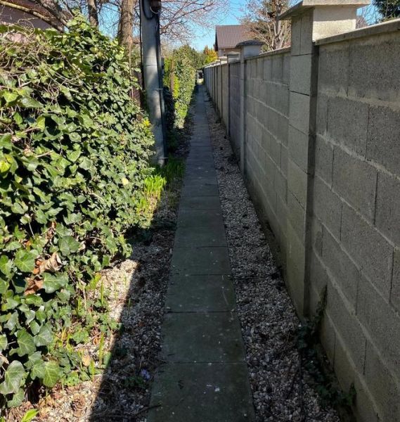 A narrow path by the wall between flowers and a fence on Hrušovská in Bratislava, Vrakuňa district, plots - residential area.