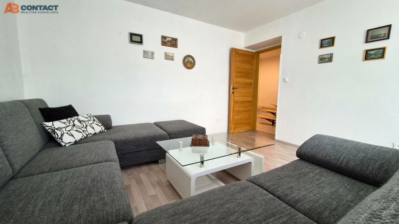 Living room in a two-room apartment with a sofa, glass table, and wooden decor flooring.