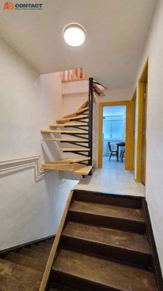 Interior of a two-story apartment with wooden stairs and an entrance to a room.