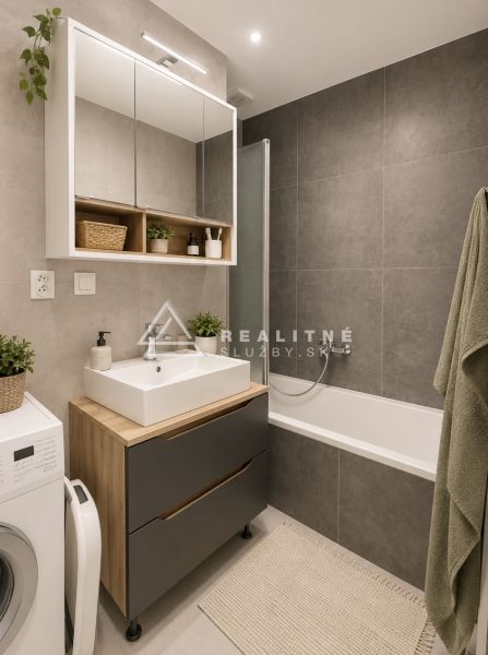 Bathroom in a 2-room apartment with a bathtub, cabinets, and a washing machine, gray tiles.