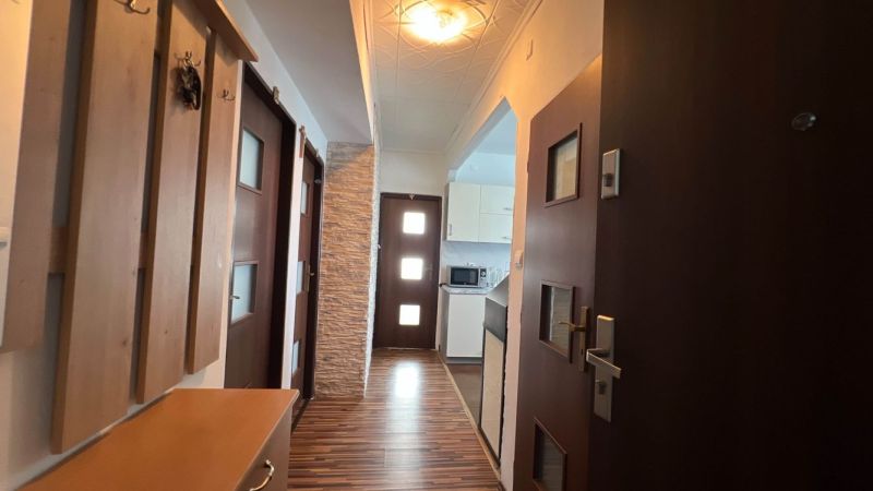 Entrance hallway in a 3-room apartment with a wooden decor floor and a kitchen in the background.