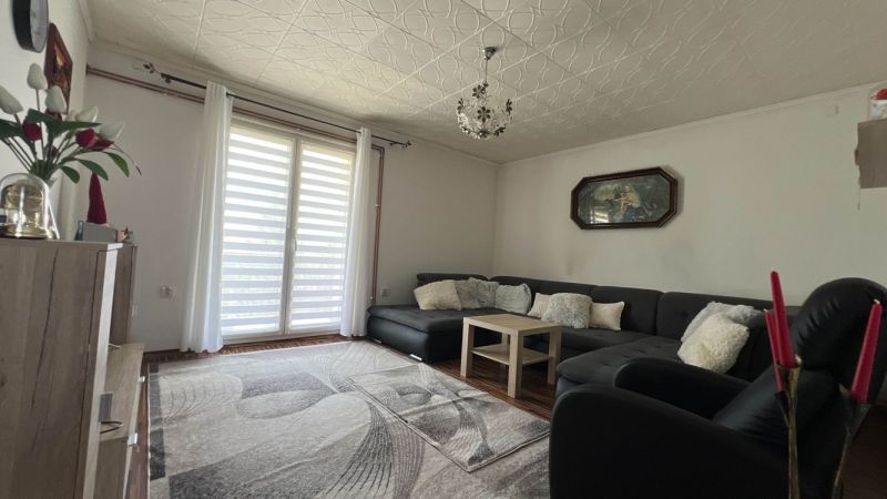 Living room in a 3-room apartment with a large sofa, wooden decor flooring, and decorations.