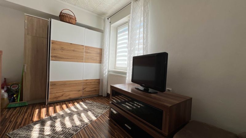 A room in a 3-room apartment with a dresser, a television, and a floor with a wood decor.