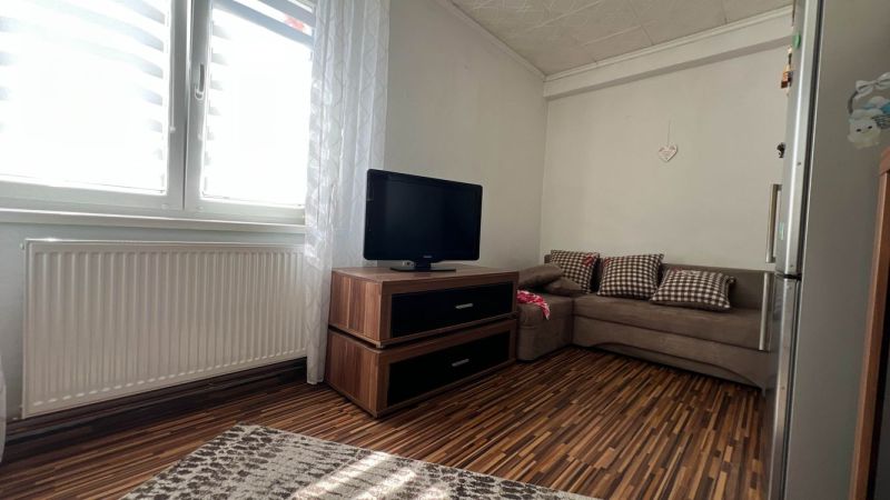 Living room with wood-patterned flooring, sofa, television, and radiator in a 3-room apartment.