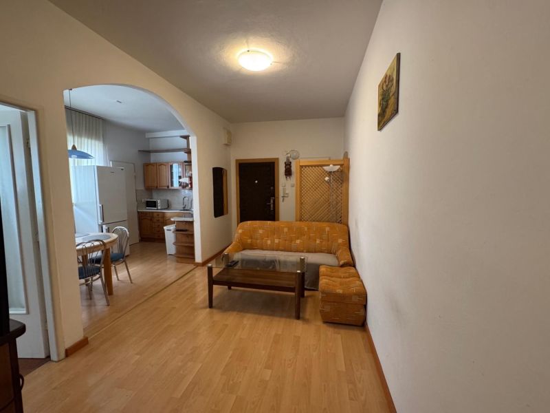 A room in a 3-room apartment with a wood-decor floor, a sofa, and a kitchenette.