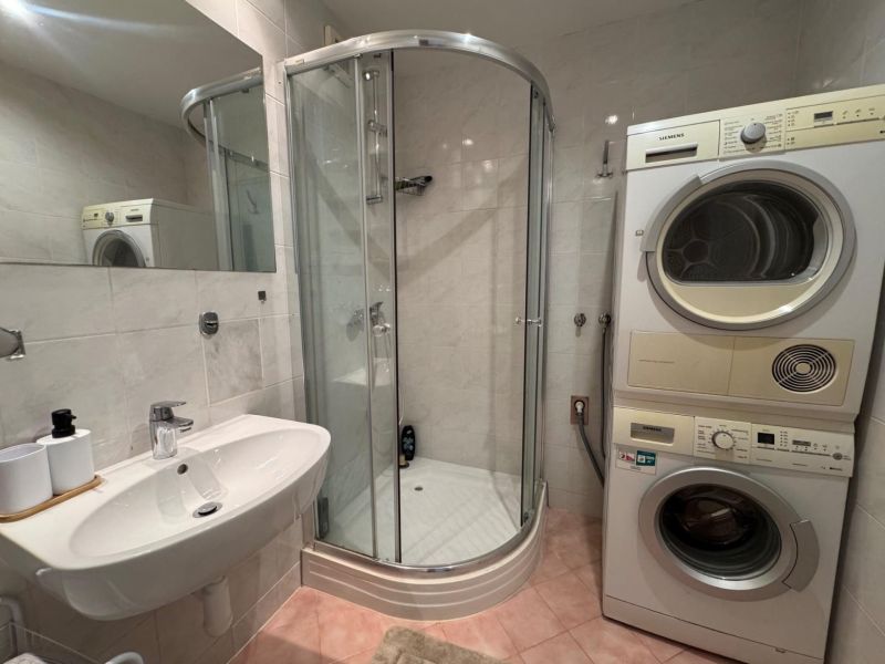 A bathroom with a washing machine, dryer, and shower in a 3-room apartment.