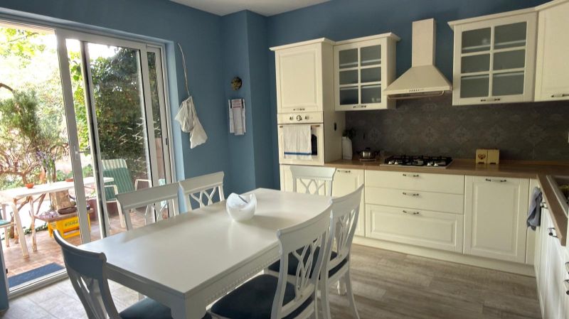 A kitchen in a family house with white furniture and access to the terrace.