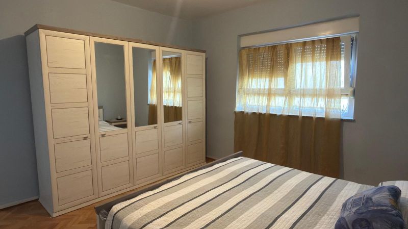 Bedroom in a family house with a bed, wardrobe, and window with sheer curtains.