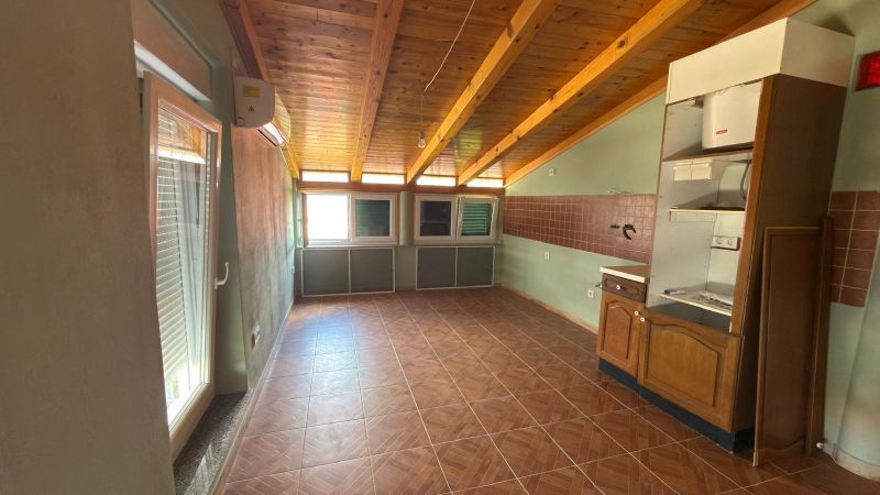 A room with a wooden ceiling, a floor with a wooden decor, and kitchen cabinets.