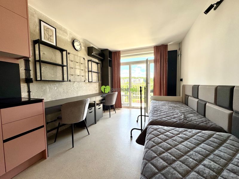 Studio apartment with beds, work desks, modern decor, and a balcony view.