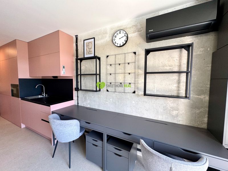 A studio apartment with a wooden decor floor, a pink kitchen, and gray work chairs.