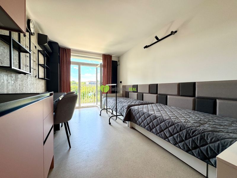 Studio apartment with two beds, a work desk, and a view through a large window.