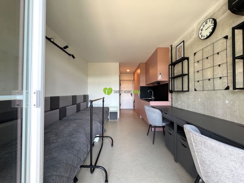 Studio apartment interior with a bed, table, and kitchenette in soft colors.