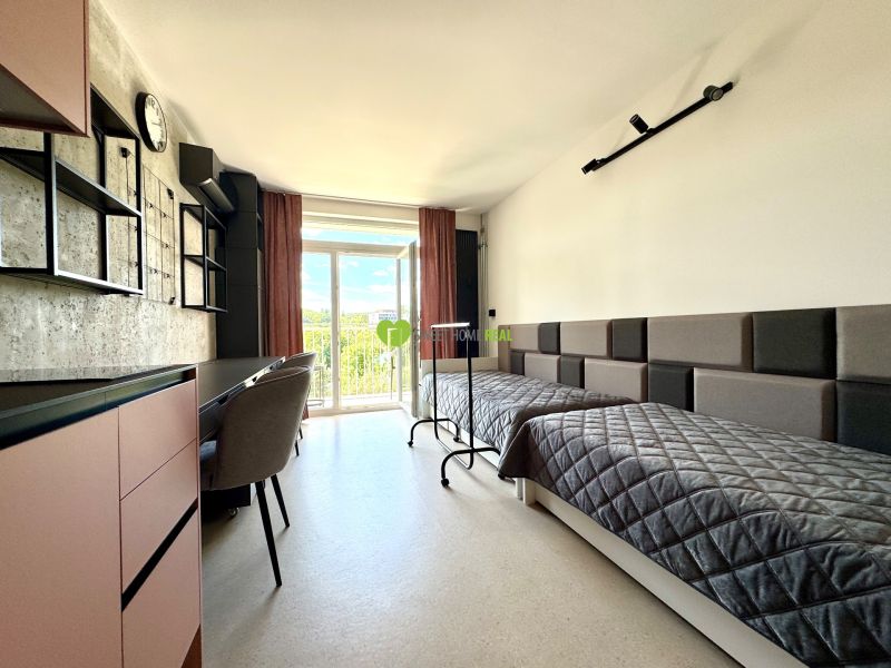 Studio with two beds, a work desk, and a view through a large window.
