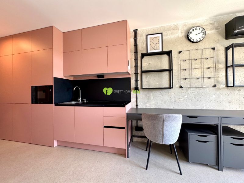 A kitchen and a work corner in a studio apartment with modern shelves and a clock on the wall.