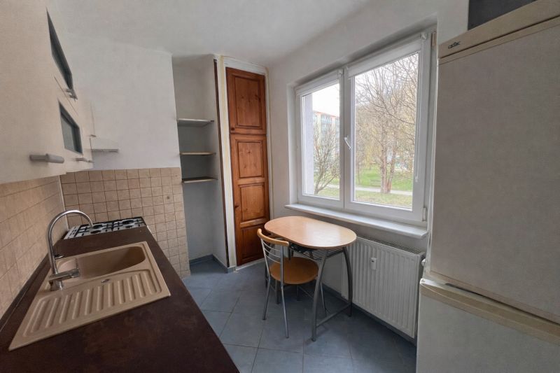A kitchen in a 2-room apartment with wooden cabinets and a table by the window.