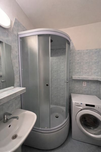 A bathroom with a shower and a washing machine in a 2-room apartment.