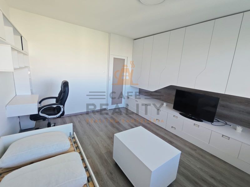 Interior of a 1-bedroom apartment with a desk, television, and wood-patterned flooring.