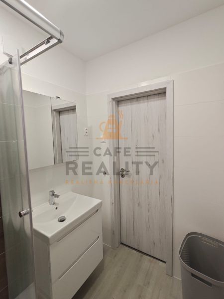 Bathroom in a studio apartment with a white sink and shower, floor with wood decor.