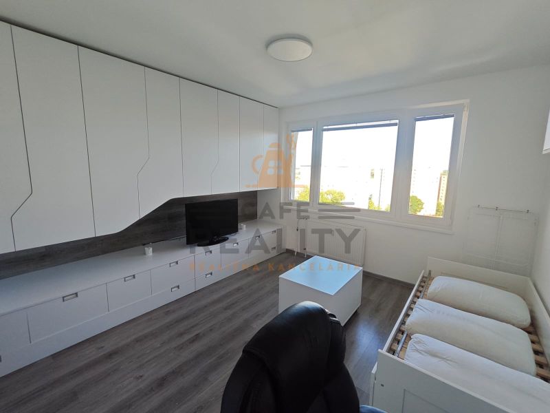 Interior of a 1-room apartment with white cabinets, wood-patterned flooring, and large windows.