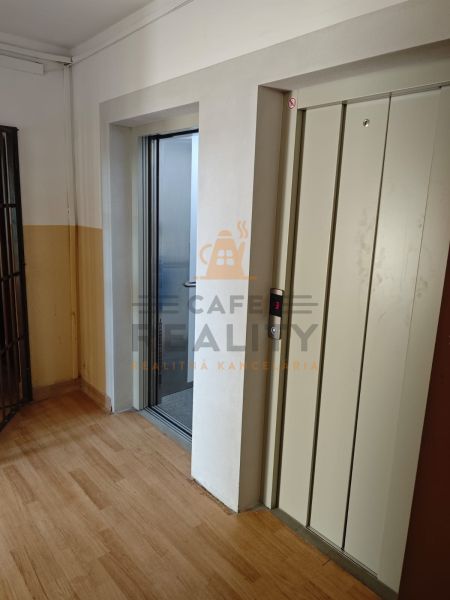 A hallway with an elevator and a floor with a wooden decor in a studio apartment.