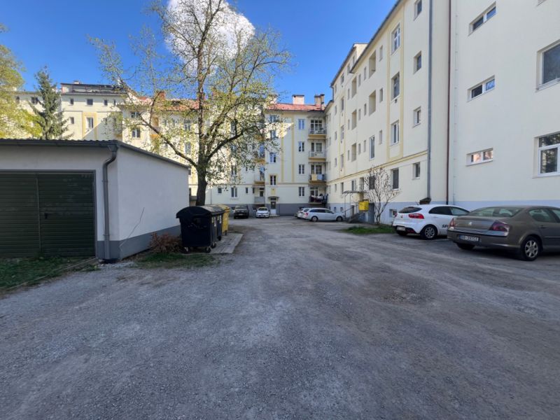 Parking lot near an apartment building in Banská Bystrica with cars and trees.