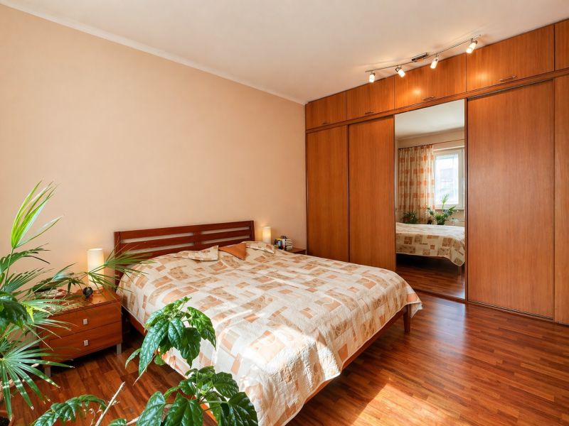 A bedroom with wood-patterned flooring, a built-in wardrobe, and a bed in a 4-room apartment.