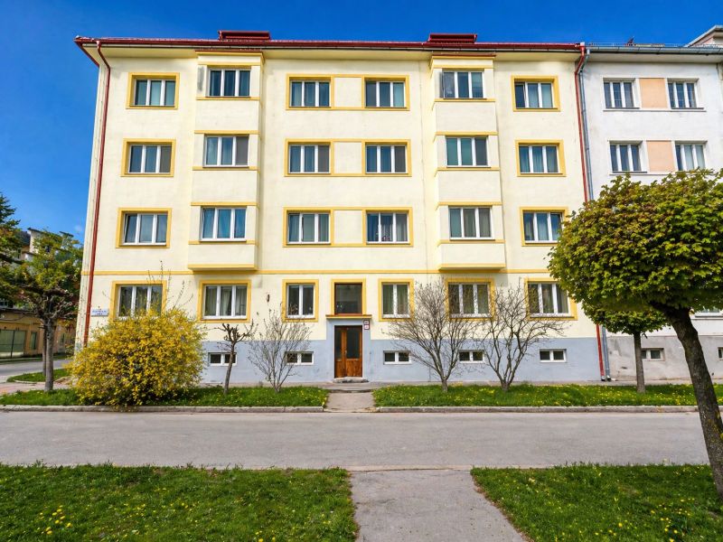 Apartment building in Banská Bystrica, yellow facade, landscaped greenery, clear sky.