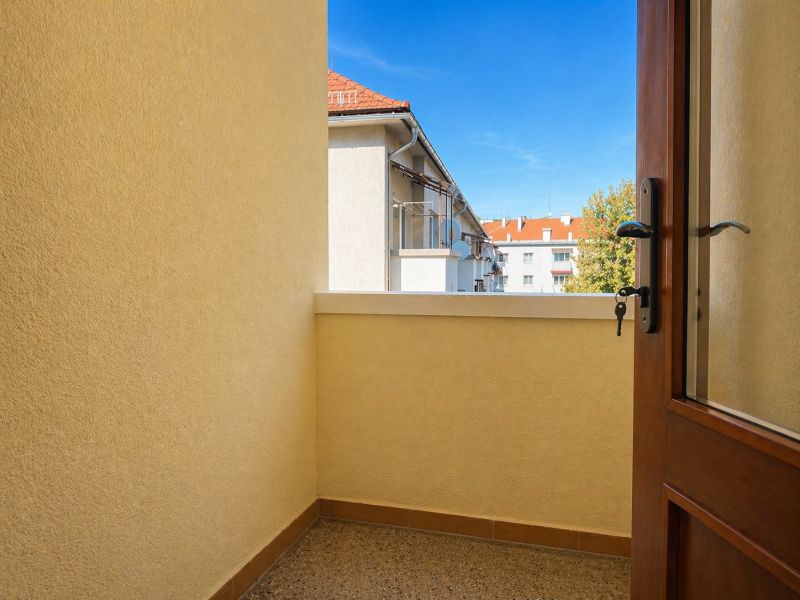 A balcony in a 4-room apartment with a view of rooftops and trees.