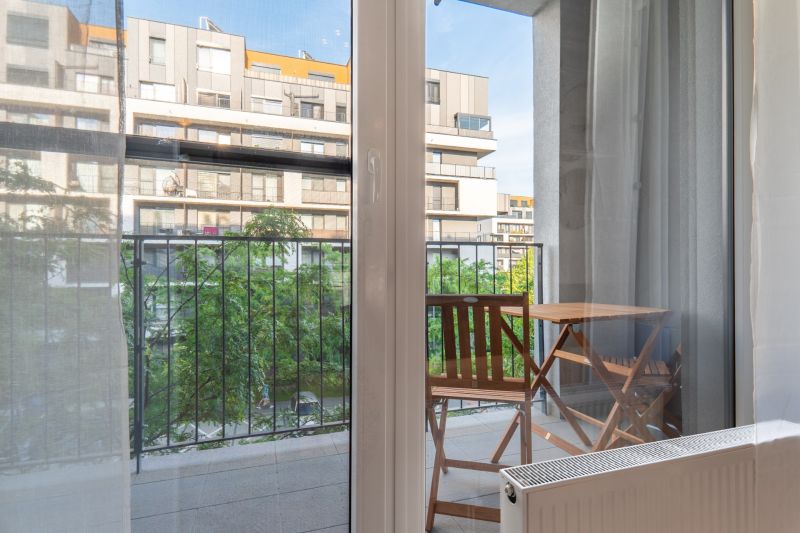 View from a 1-bedroom apartment to a balcony with a table and chairs.