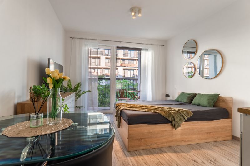 Bright 1-room apartment with a bed, mirrors, and wooden decor flooring, balcony outside the window.