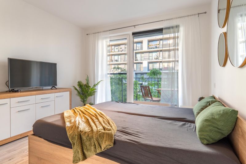 A bedroom in a studio apartment with a television, mirrors, and a balcony, wooden decor flooring.