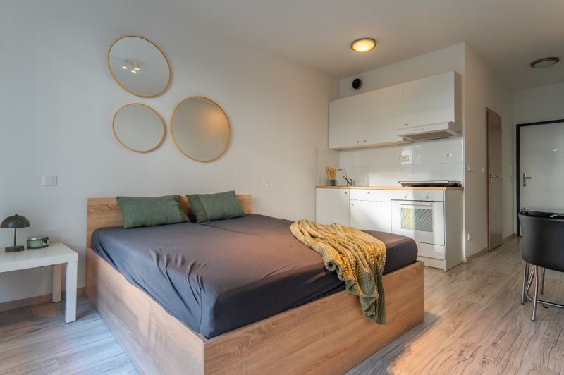 A simple room with a bed, a kitchenette, and a wooden decor floor.