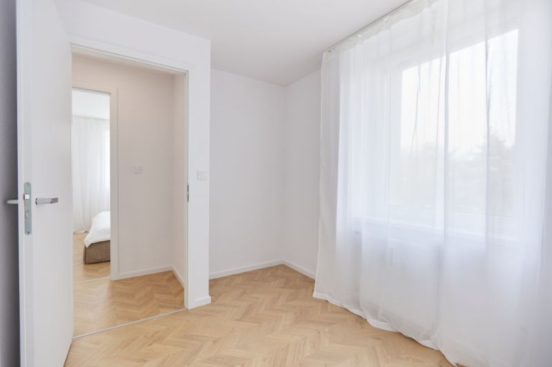 A room with white curtains and a wooden decor floor in a 4-room apartment.