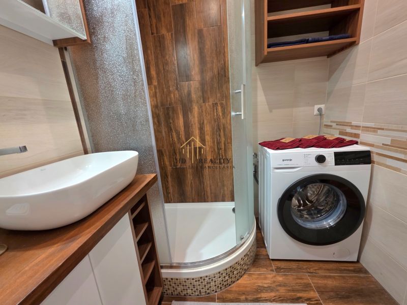 Bathroom in a 2-room apartment with a washing machine and a wooden decor floor.