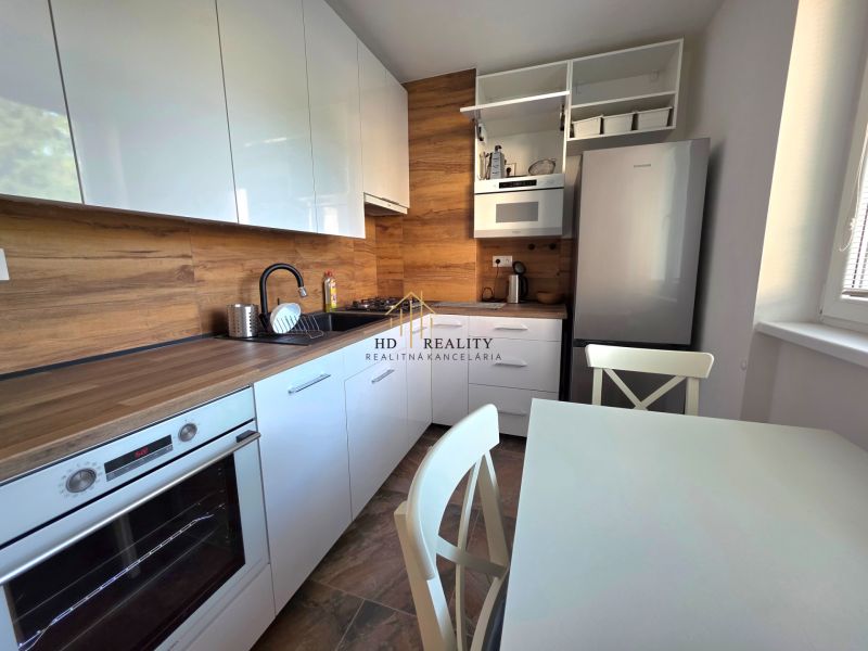 A kitchen with white cabinets and appliances, equipped with wood-patterned flooring in a 2-room apartment.