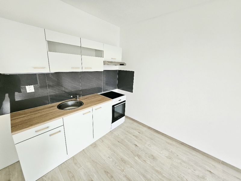 White kitchen unit with black tiles in a studio apartment with a wood-patterned floor.