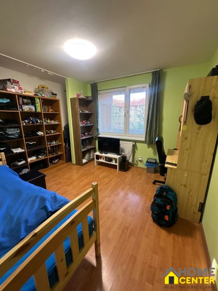 A room in a 3-room apartment with shelves, a bed, and a wooden decor floor.