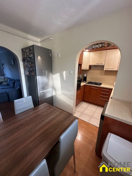 A kitchen with wooden decor, a dining table, a refrigerator, and an arch leading to the living room.