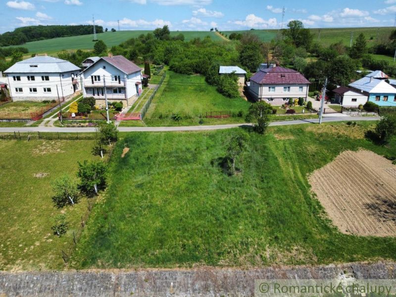 Lands - housing in Karna: green areas, houses, and an access road under the blue sky.