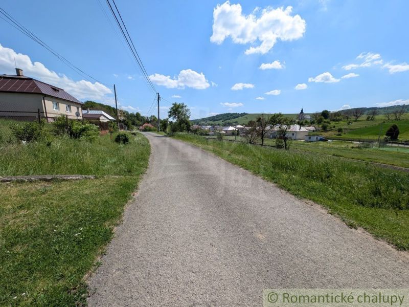 A path surrounded by grass leads through a rural area in Karna with a view of houses.
