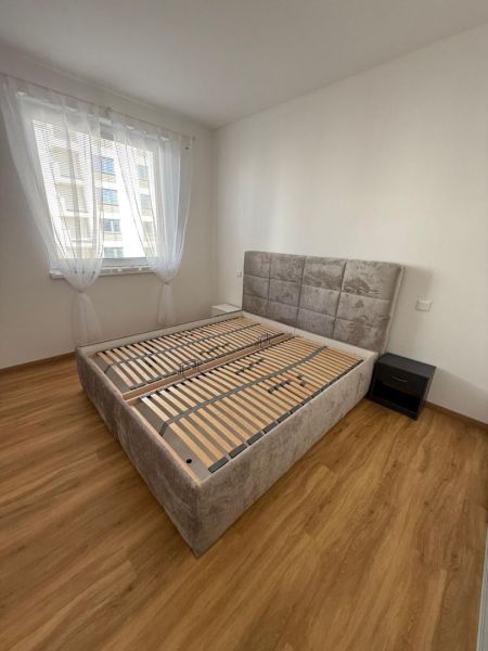 Bedroom in a two-room apartment with a wood-patterned floor and a large bed.