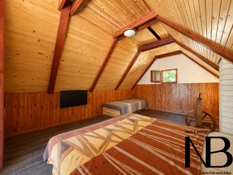 The attic in the cottage with wooden decor offers a bed and a television.