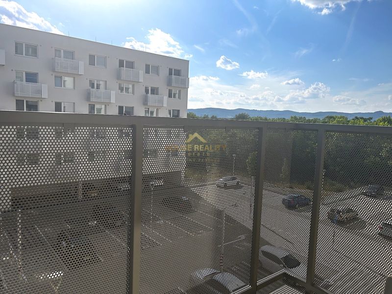 A balcony in a one-room apartment with a view of the parking lot and surrounding mountains.