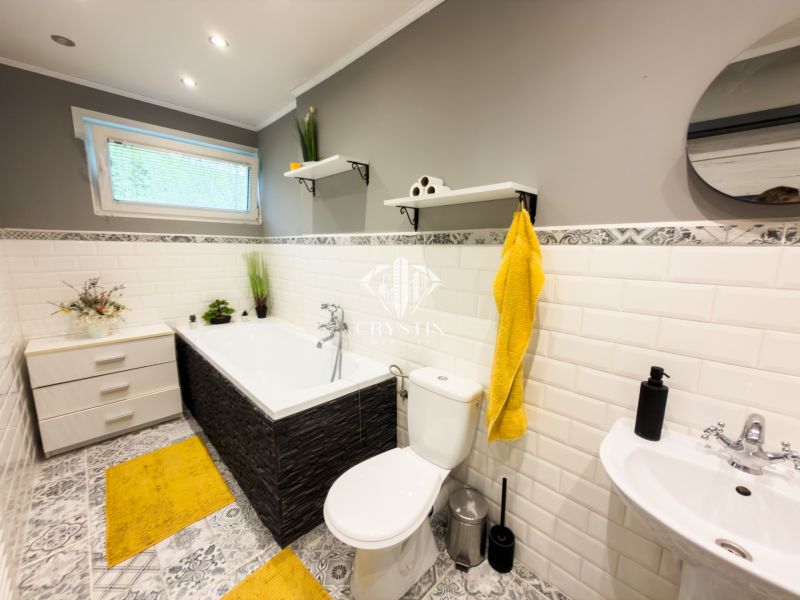 A bathroom in a family house with tiles, a bathtub, and yellow accessories.
